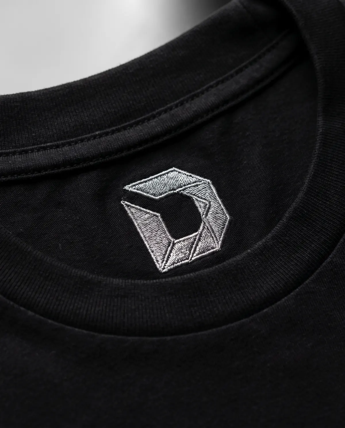 Inside the back neck: the D embroidered in steel-grey thread.