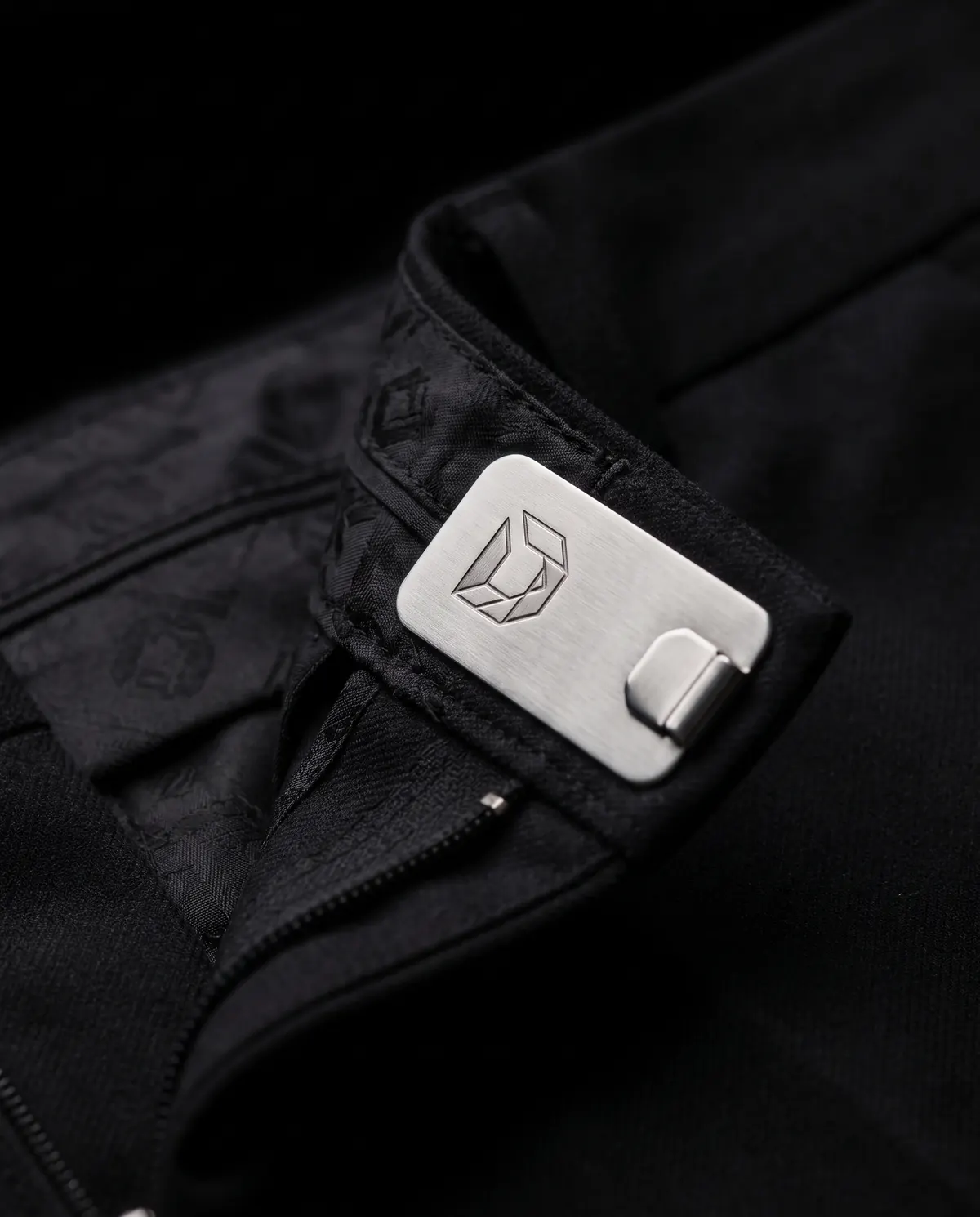 Close up of the pleated trouser: the waistband hook, in stainless steel.